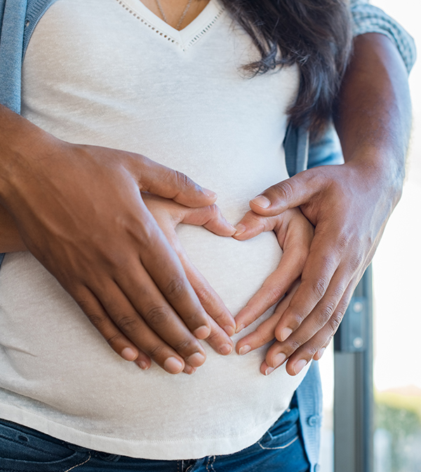 Man and woman with hands in heart shape on pregnant woman's stomach